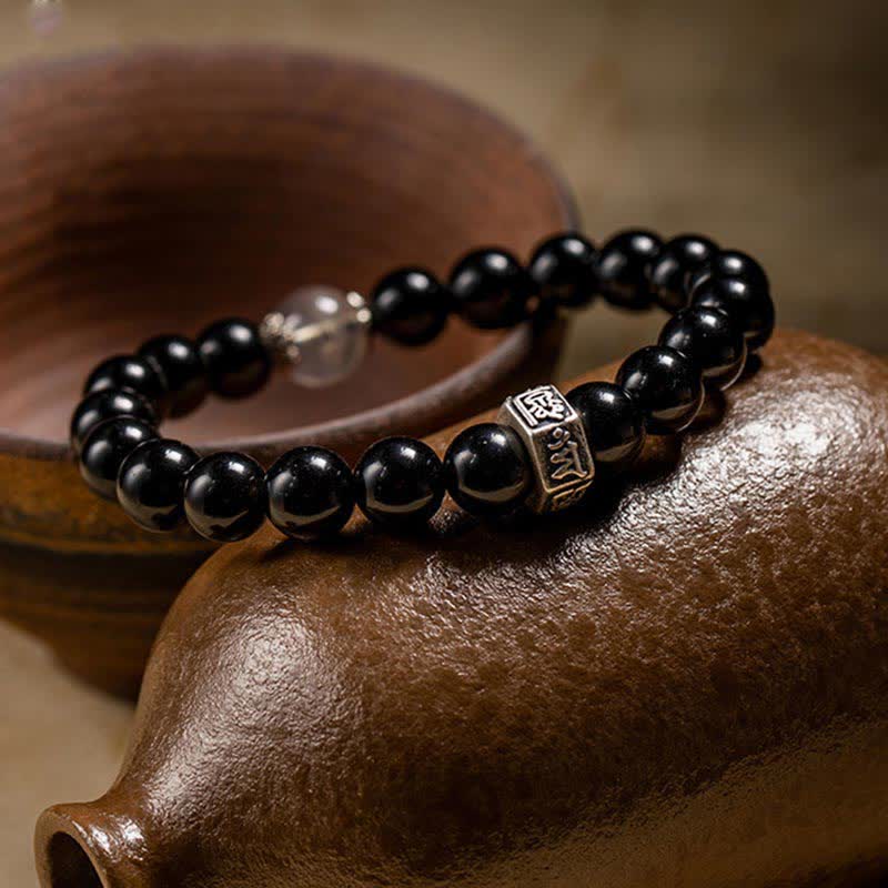 Schwarzes Obsidian Armband mit silbernem Charm auf Holzoberfläche elegant.