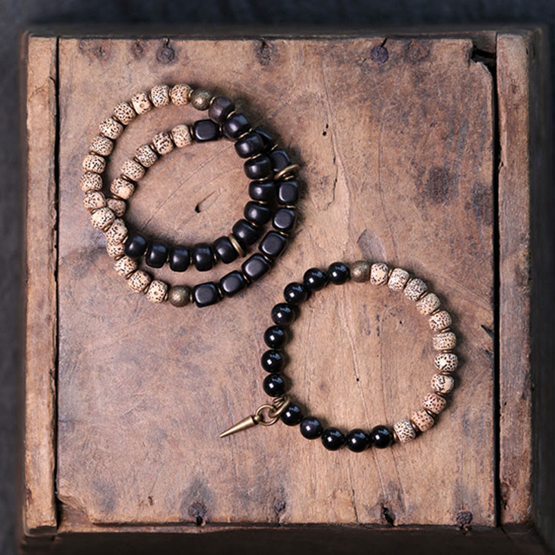 Zwei Armbänder mit schwarzem Obsidian und kupferfarbenen Perlen auf Holz.
