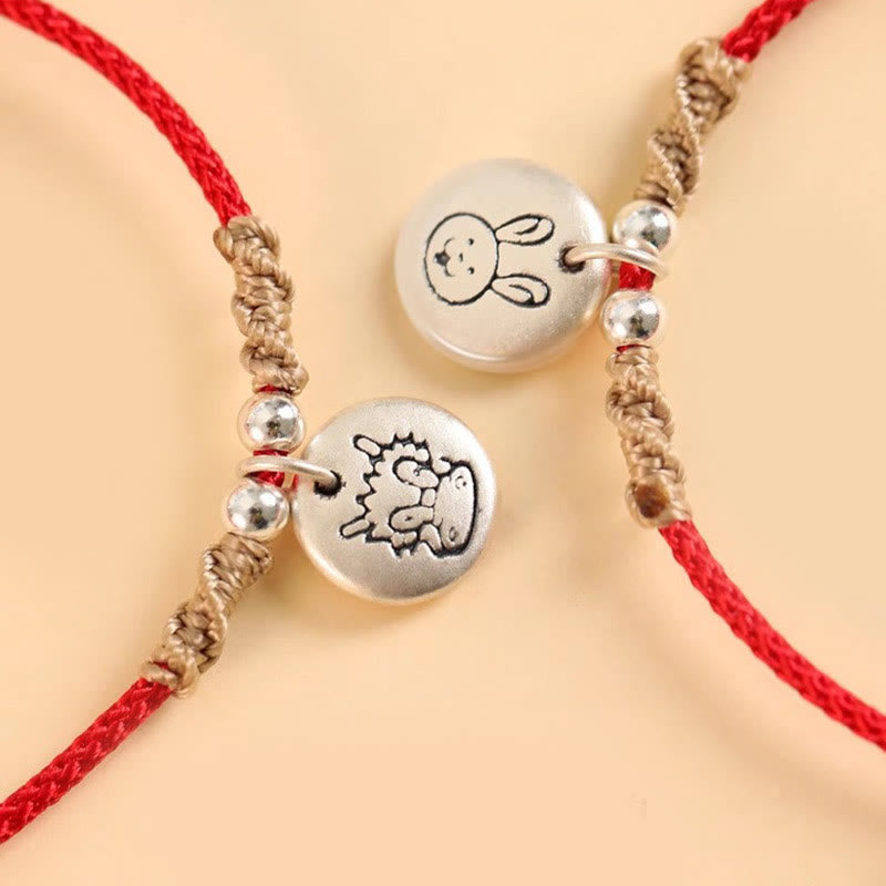 Silbernes Armband mit chinesischen Tierkreiszeichen auf cremefarbenem Hintergrund.