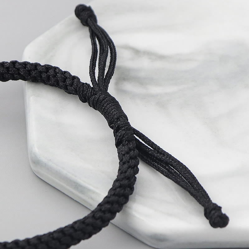 Schwarzes Armband mit Seilknoten auf weißem Marmor Hintergrund.