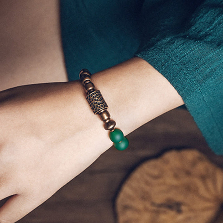 Armband mit grünem Stein und bronzefarbenen Perlen am Handgelenk getragen
