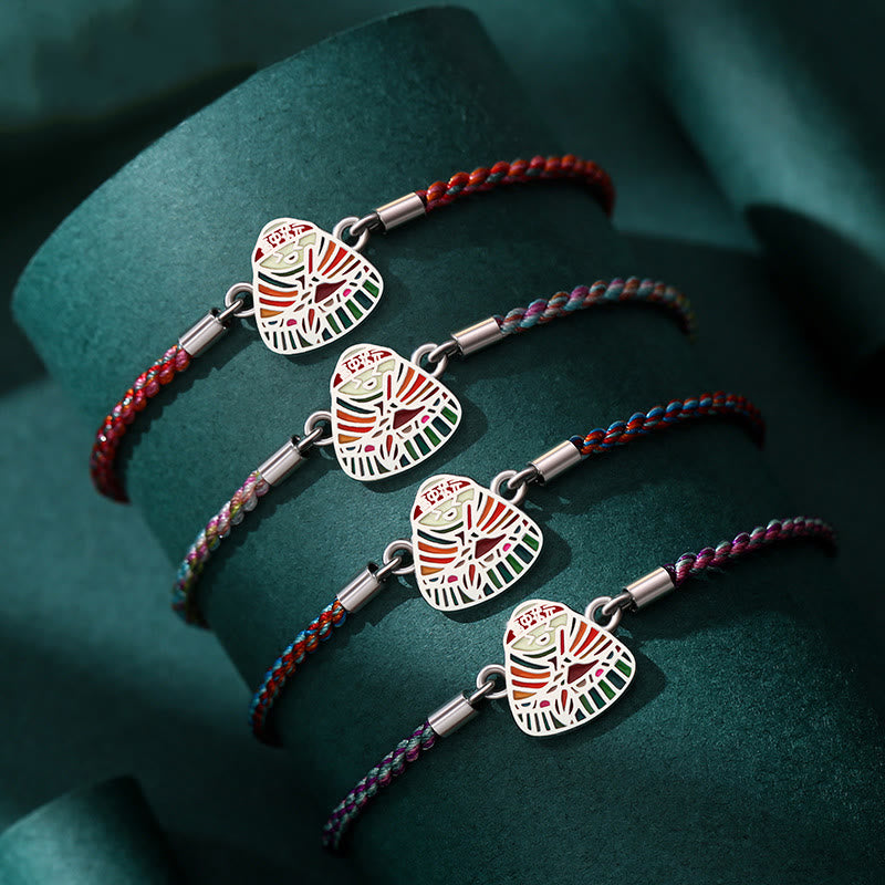 Vier farbige Armbänder mit silbernen Glücksbringer-Anhängern auf grünem Untergrund.