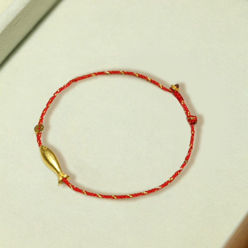 Rotes Armband mit goldenem Koi Fisch Anhänger auf heller Oberfläche.