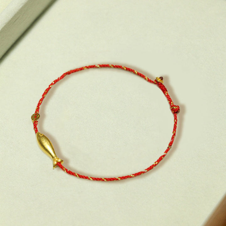 Rotes Armband mit goldenem Koi Fisch Anhänger auf heller Oberfläche.