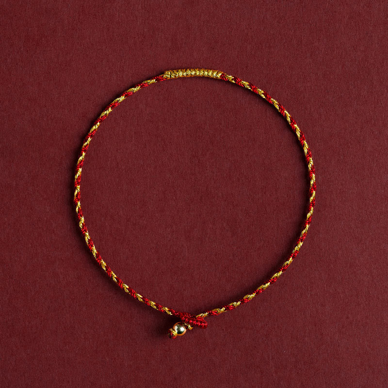Rotes goldenes geflochtenes Armband mit Knoten auf burgunderrotem Hintergrund.