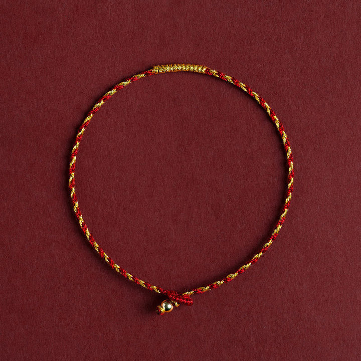 Rotes goldenes geflochtenes Armband mit Knoten auf burgunderrotem Hintergrund.