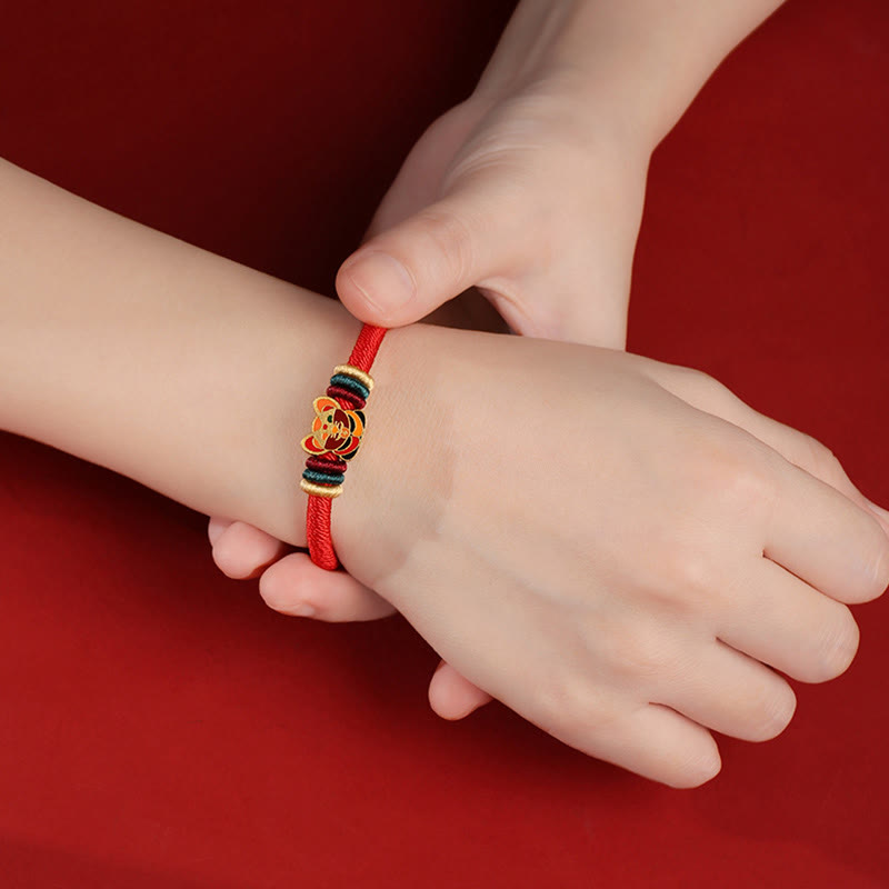 Rotes Armband mit goldenen Charms am Kinderpuls getragen.