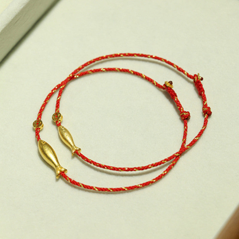 Rotes Armband mit goldenem Koi-Fisch-Anhänger auf hellem Hintergrund.