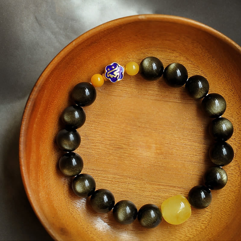Obsidian Armband mit gelben Steinen und blauem Schmuckelement auf Holzschale.