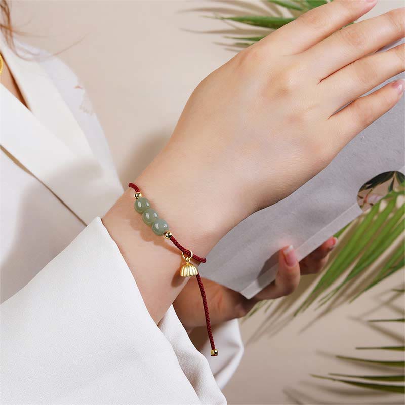 Jade Lotus Armband mit roten Kordeln und goldenem Verschluss am Handgelenk.