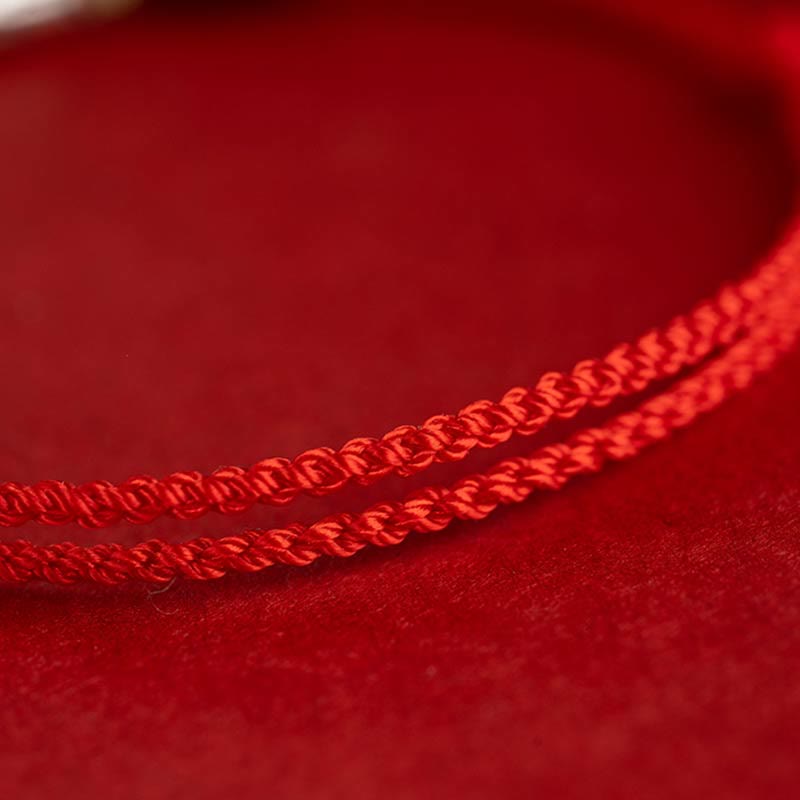 Rotes Seidenarmband mit geflochtener Schnur auf rotem Stoff.