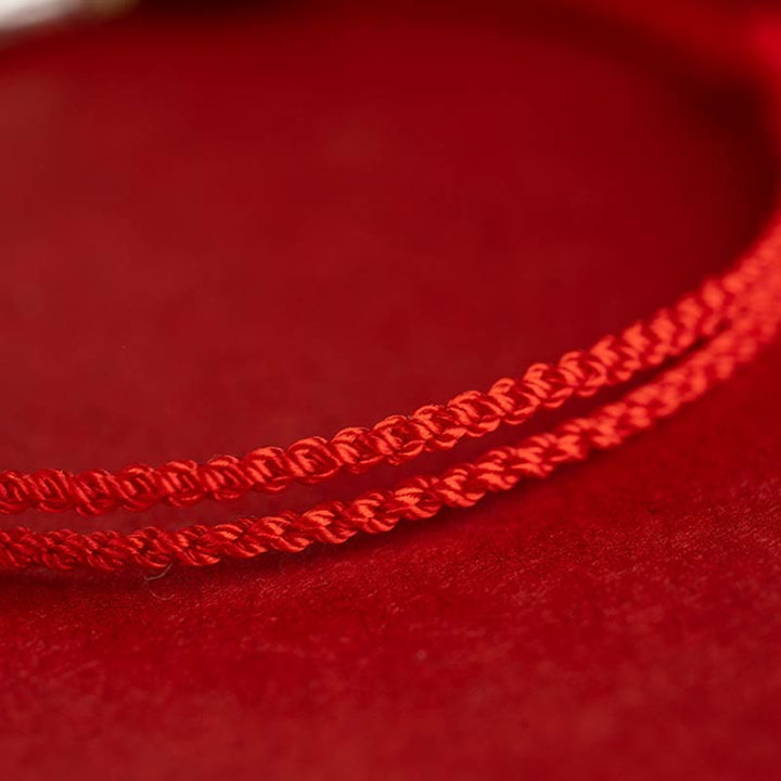 Rotes Seidenarmband mit geflochtener Schnur auf rotem Stoff.