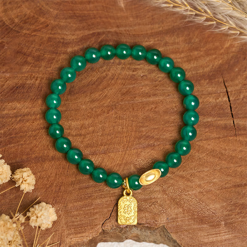 Armband Achat Fu-Zeichen grüne Perlen goldener Anhänger Holz Hintergrund