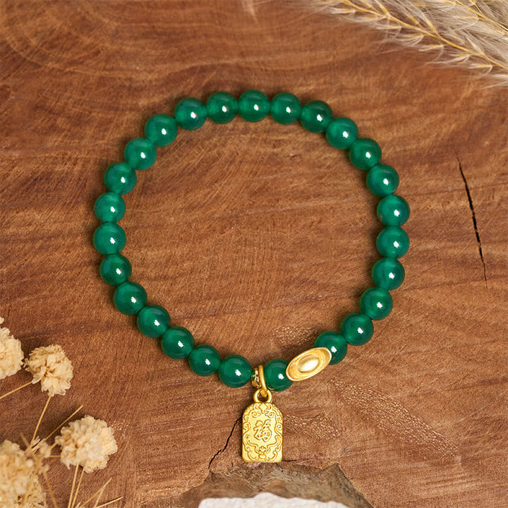 Armband Achat Fu-Zeichen grüne Perlen goldener Anhänger Holz Hintergrund