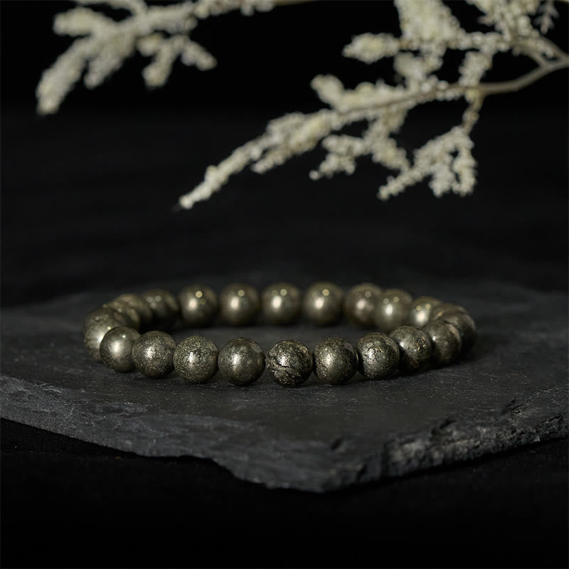 Armband Pyrit Vertrauen Wohlstand Perlen auf Schieferplatte mit weißer Blüte