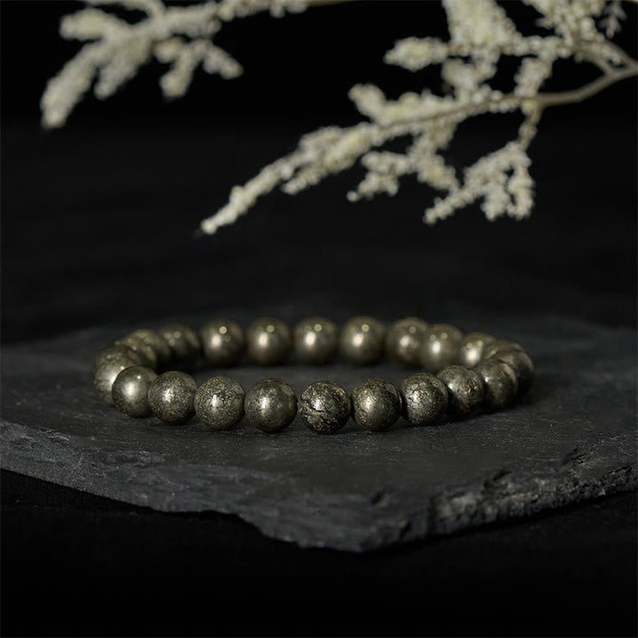 Armband Pyrit Vertrauen Wohlstand Perlen auf Schieferplatte mit weißer Blüte