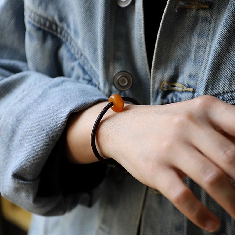 Braunes Armband mit orangem Stein elastisch am Handgelenk getragen.