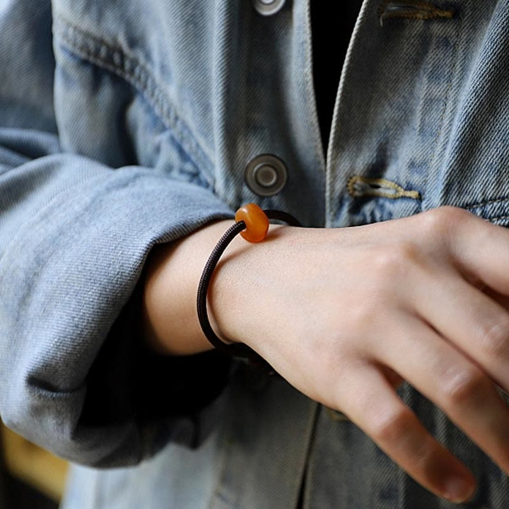 Braunes Armband mit orangem Stein elastisch am Handgelenk getragen.