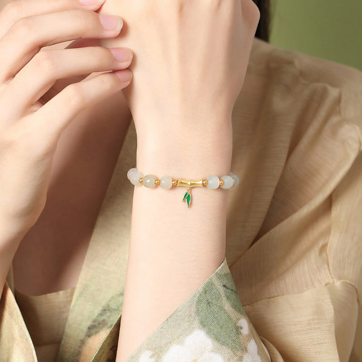 Armband mit weißer Jade und grünem Blatt-Anhänger am Handgelenk.