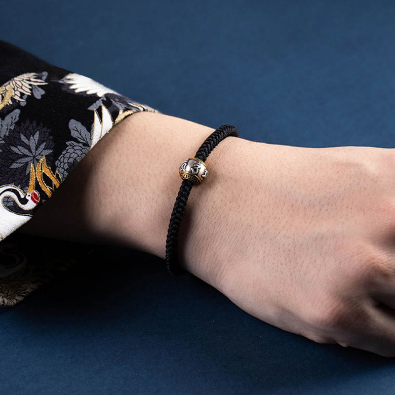 Schwarzes geflochtenes Armband mit silbernem Om Mani Padme Hum Verschluss am Handgelenk.