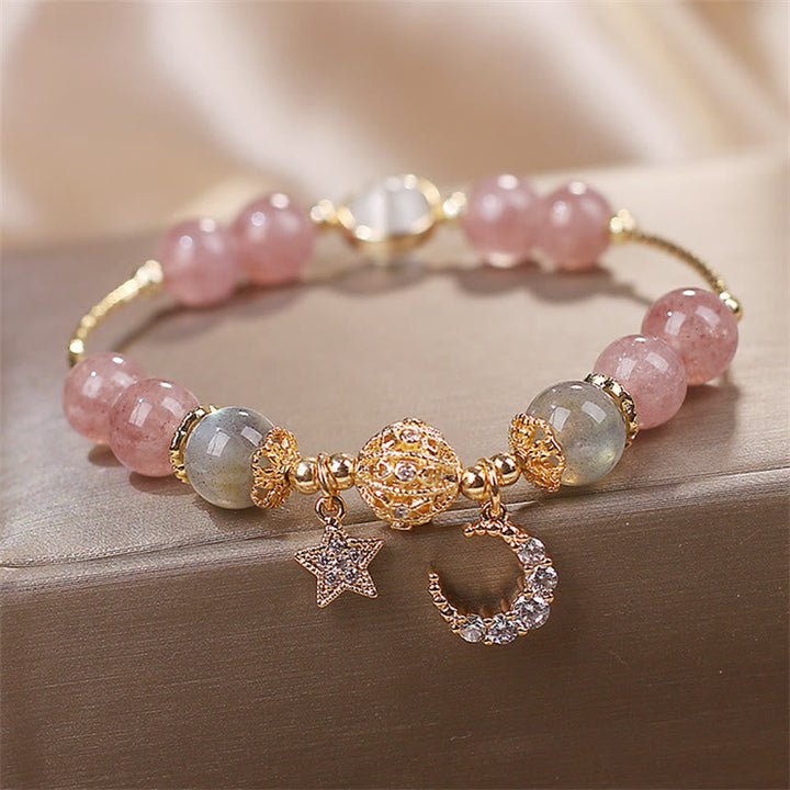 Erdbeerquarz Mondstein Armband mit Mond-Stern-Anhängern auf Holz-Oberfläche.
