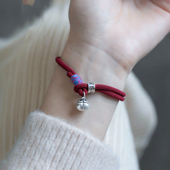 Rotes Seidenarmband mit silbernem Om Anhänger am Handgelenk getragen.
