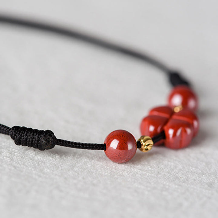 Armband Zinnober Kleeblatt rote Perlen schwarze Kordel Nahaufnahme Flat Lay
