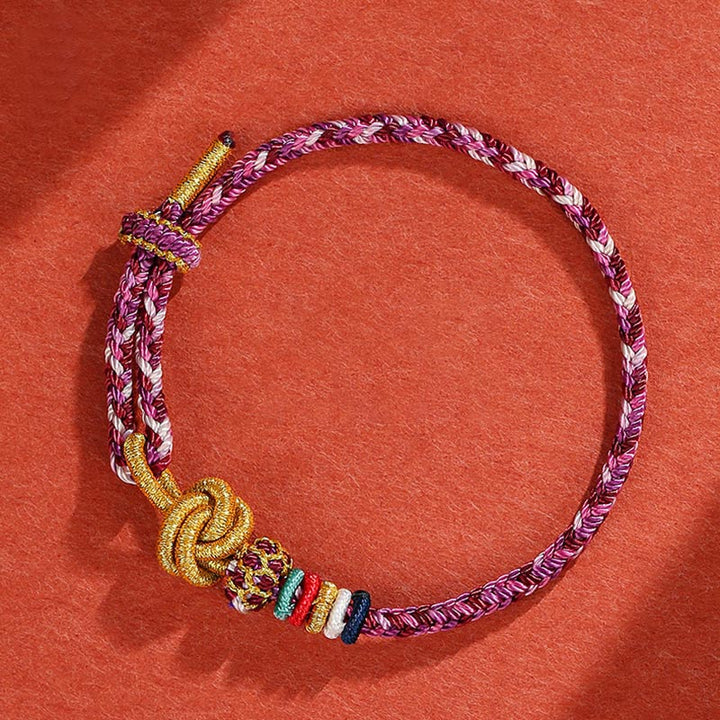 Buntes geflochtenes Armband mit goldenen Perlen auf rotem Hintergrund.