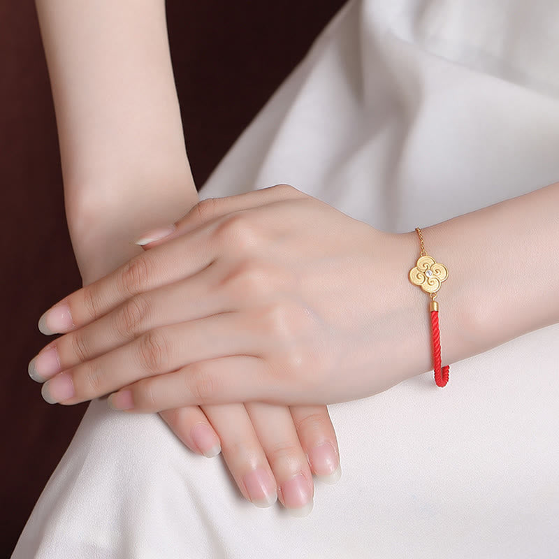 Goldenes Kleeblatt Armband mit rotem Seidenfaden elegant am Handgelenk getragen.