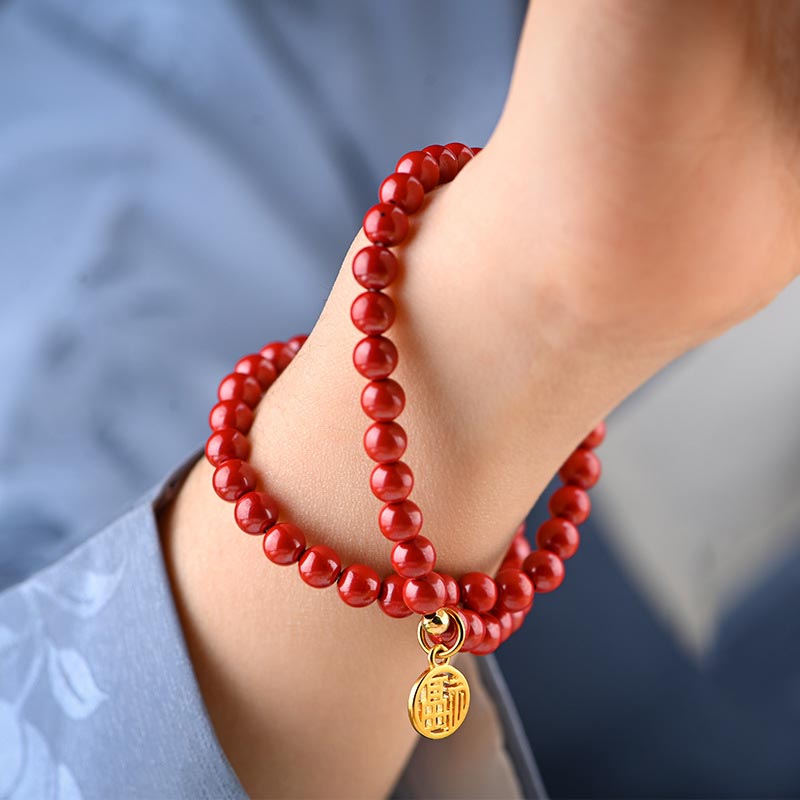 Rotes Armband Zinnober am Handgelenk mit goldenem Anhänger getragen