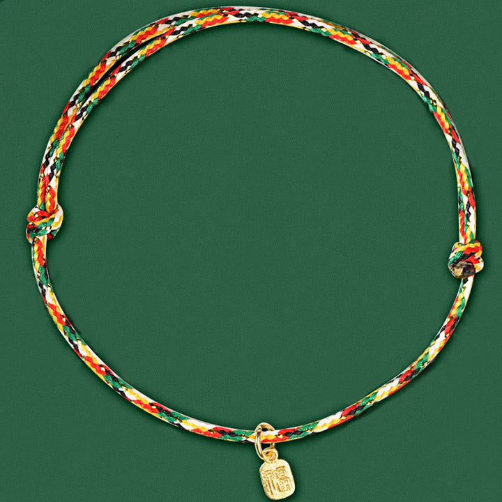 Buntes Armband Fu-Zeichen – Glück & Frieden & Energie mit Goldanhänger grünem Hintergrund.