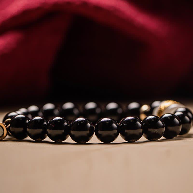 Schwarzer Obsidian Armband mit Om Symbol elegant auf neutralem Hintergrund.