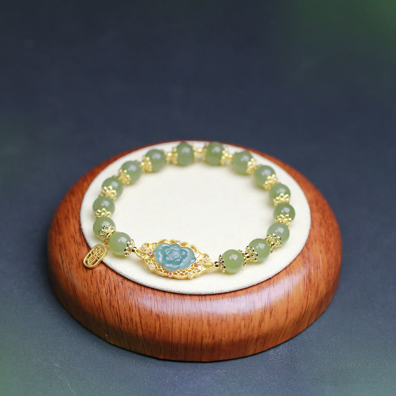Jade Armband mit goldenem Lotus-Anhänger auf Holzständer displayt.