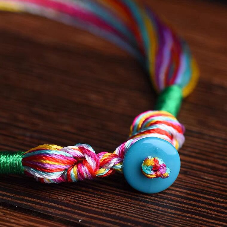 Buntes Fünffarben Armband mit blauer Perle auf Holzoberfläche Schutz.