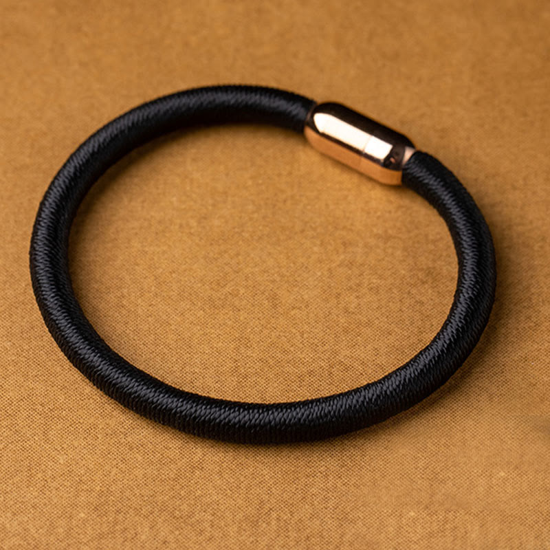Schwarzes elastisches Armband mit Magnetverschluss auf beigem Hintergrund.
