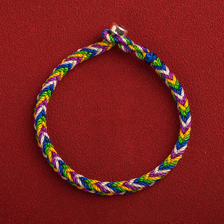 Buntes geflochtenes Armband mit Glück Charm auf rotem Hintergrund.