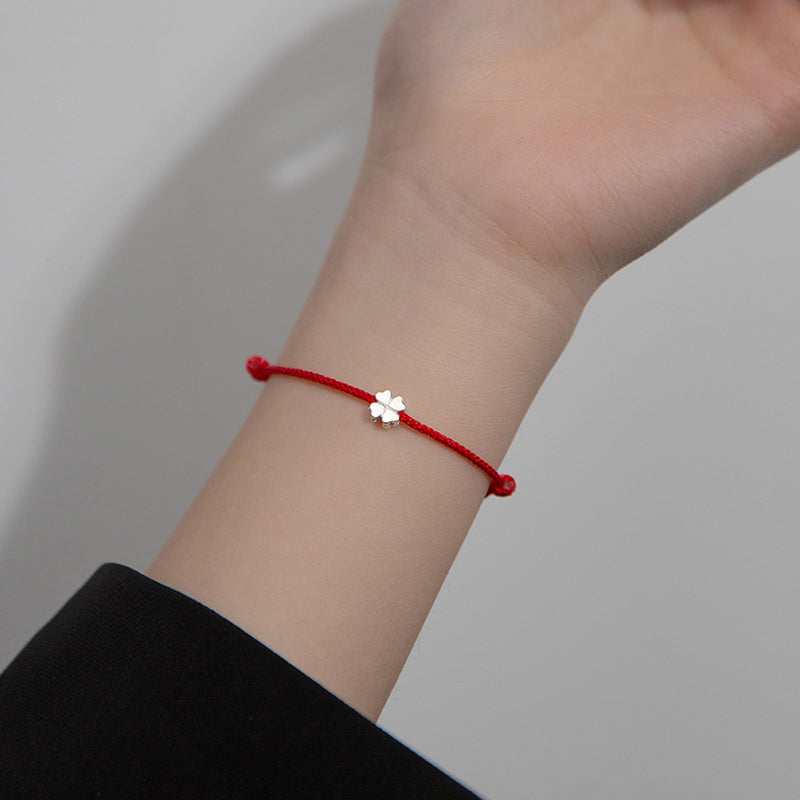 Rotes Armband mit silbernem Kleeblatt Charm am Handgelenk getragen