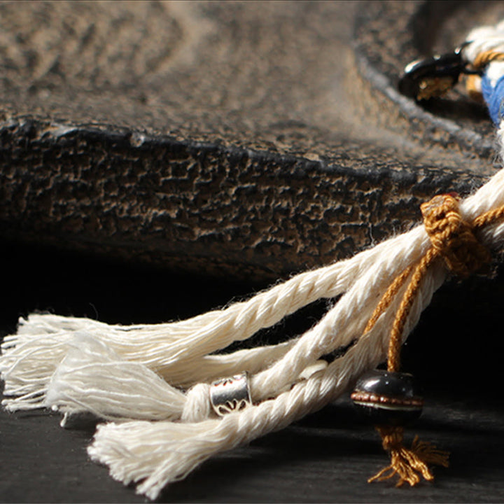 Armband – Glück & Wohlstand & Stärke am Handgelenk mit weißer Schnur getragen.