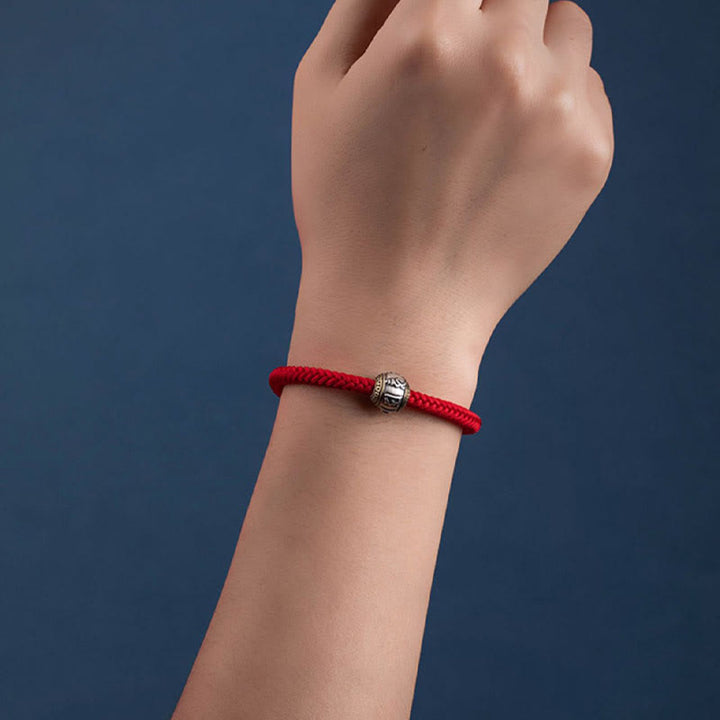 Rotes Armband mit silbernem Om Mani Padme Hum Anhänger am Handgelenk getragen