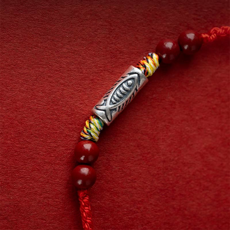 Rotes Armband mit silbernem Fischanhänger und Perlen elegantly displayed.