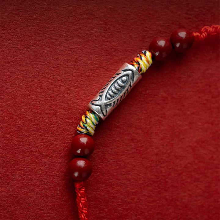 Rotes Armband mit silbernem Fischanhänger und Perlen elegantly displayed.