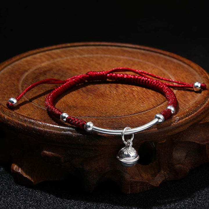 Rotes Schnur Armband mit Silberglocke auf Holzplatte Flat Lay