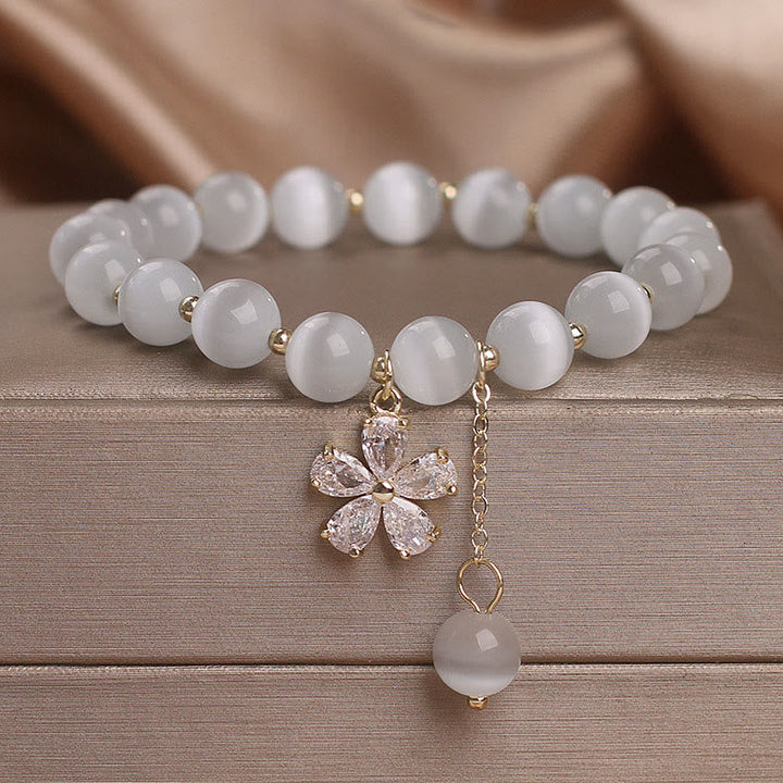 Weißes Jade Armband mit Blütenanhänger auf Holzoberfläche.