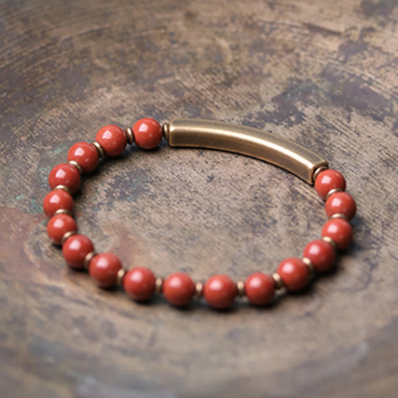 Rotes Perlen Armband mit Bronzeröhrchen auf strukturiertem Hintergrund Nahaufnahme