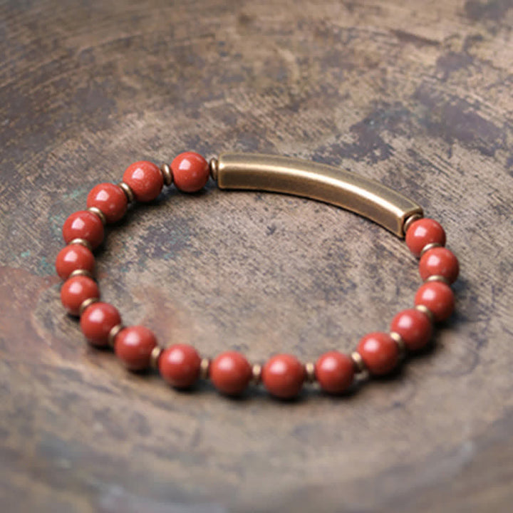 Rotes Perlen Armband mit Bronzeröhrchen auf strukturiertem Hintergrund Nahaufnahme