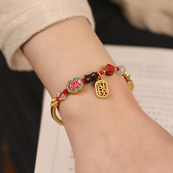 Armband Auspicious mit roten Perlen und goldenen Anhängern elegant getragen.