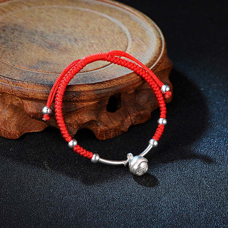 Rotes Schnur Armband mit Glocke und Silberperlen auf Holz