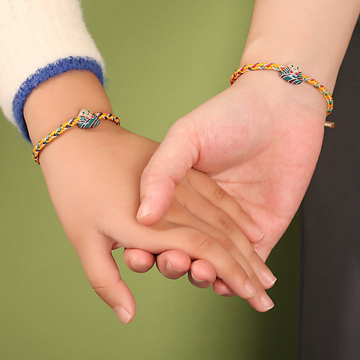 Zwei Kinder halten Hände mit bunten Glücksbändern am Handgelenk zusammen.