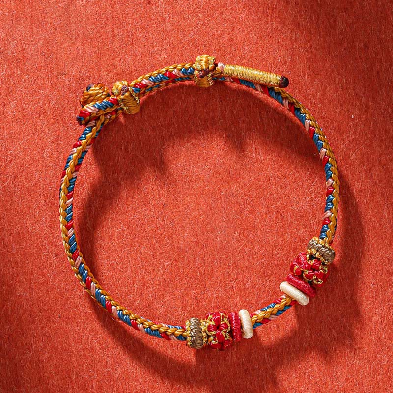 Geflochtenes rotes Schnur Armband mit goldenen Perlen auf rotem Hintergrund Flat Lay