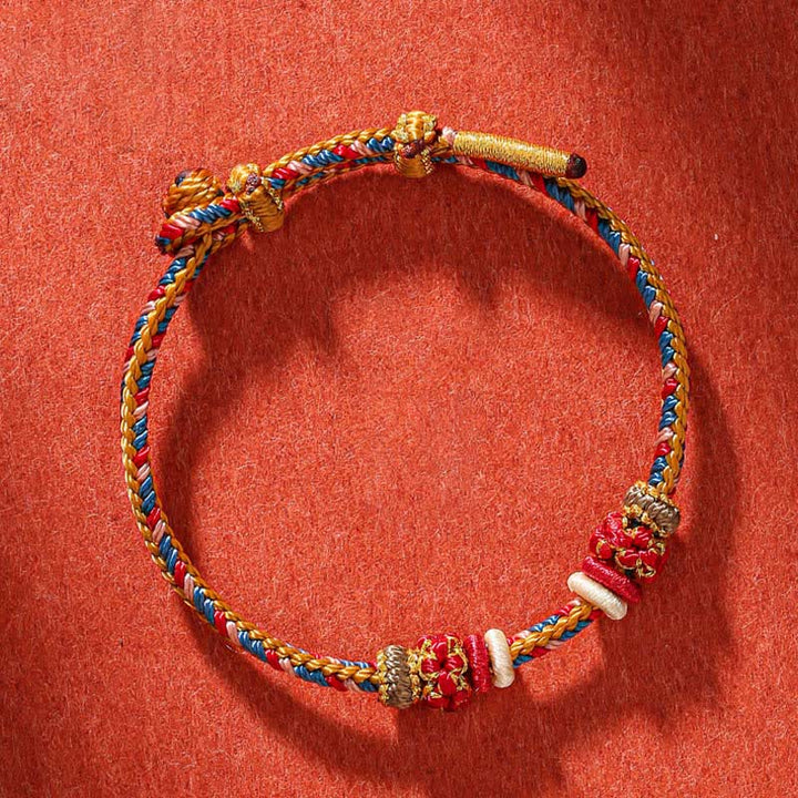 Geflochtenes rotes Schnur Armband mit goldenen Perlen auf rotem Hintergrund Flat Lay